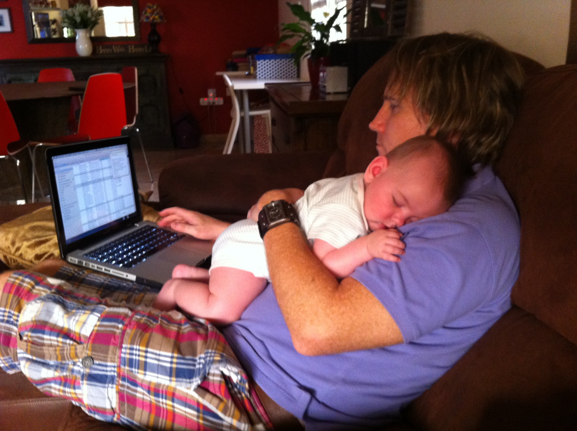 Stefan holding his sleeping baby daughter while using a laptop